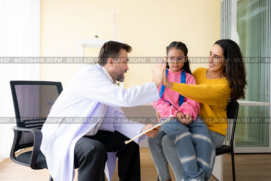 Doctor giving high five to a mom of little girl while sitting on mother’s lap at hospital. Стоковое фото, агентство Ingram Publishing / Фотобанк Лори
