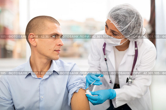 Doctor in a protective mask injects a vaccine to a man with syringe. Стоковое фото, фотограф Яков Филимонов / Фотобанк Лори