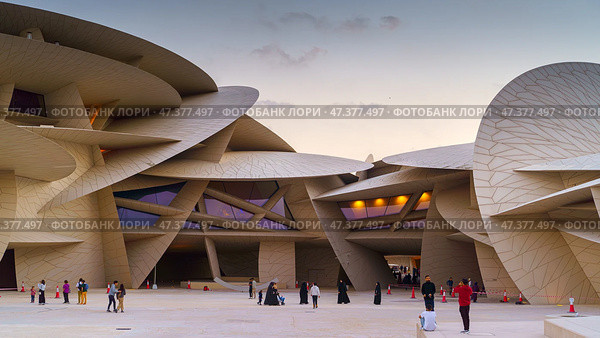 Doha, Qatar - Jan 06 2024, a panoramic view of National Museum of Qatar courtyard, patio, with some people in it, in shape of desert rose, at evening, Doha, Qatar. Редакционное фото, фотограф Сергей Богомяко / Фотобанк Лори
