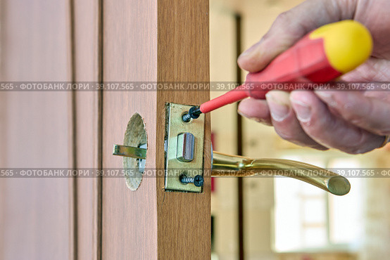Door latch plate is fastened with fixing screw, locksmith tightens fastener with screwdriver. Стоковое фото, фотограф Владимир Григорьев / Фотобанк Лори