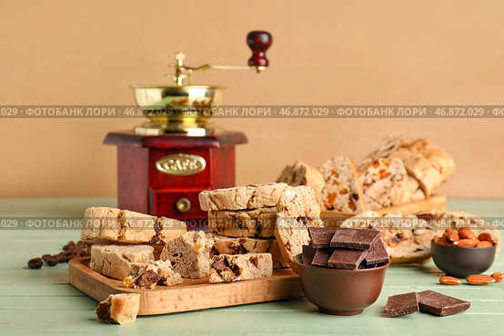 Доска с вкусным печеньем бискотти, миндалем, шоколадом и кофемолкой на цветном деревянном столе. Стоковое фото, фотограф Pixel_shot / Фотобанк Лори