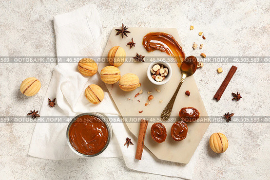 Доска с вкусным печеньем в форме ореха, варёной сгущёнкой и ингредиентами на белом шершавом столе. Стоковое фото, фотограф Pixel_shot / Фотобанк Лори
