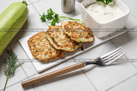 Доска с вкусными кабачковыми оладьями с сметаной на белом плиточном фоне. Стоковое фото, фотограф Pixel_shot / Фотобанк Лори