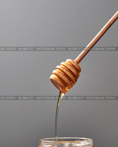 Dripping sweet honey into a jar with fresh organic syrup on a gray background, place for text. Jewish rosh hashanah holiday concept.. Close up of wooden stick with dripping sweet natural honey on a gray background, traditional useful sweetness. Стоковое фото, агентство Ingram Publishing / Фотобанк Лори
