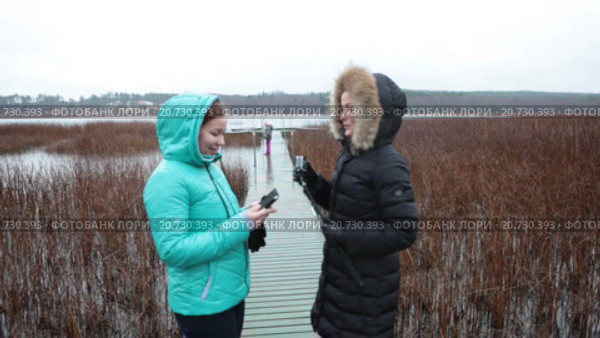 Две симпатичные женщины гуляют по берегу озера и фотографируют на телефон и экшн камеру. Стоковое видео, видеограф Кекяляйнен Андрей / Фотобанк Лори