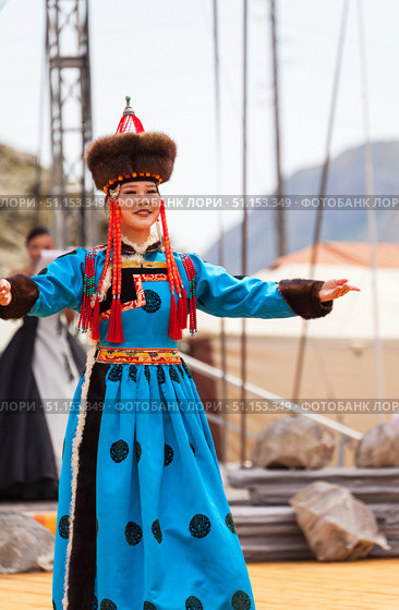 ELANTSY, IRKUTSK REGION, RUSSIA - July 5, 2025: Erdynskie Games– festival of nomadic peoples of Eurasia. A beautiful Buryat girl in national blue costume and fur hat greets guests on an open stage. Редакционное фото, фотограф Виктория Катьянова / Фотобанк Лори