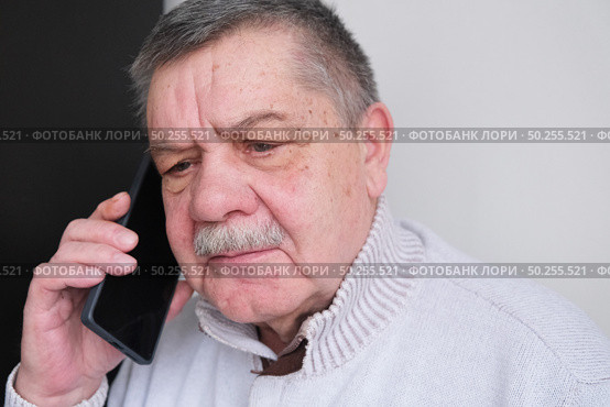 Elderly man is talking on a smartphone. A tired, distrustful, shocked pensioner who feels uncomfortable listening to an unknown caller making questionable requests. Стоковое фото, фотограф Терехова Марина / Фотобанк Лори