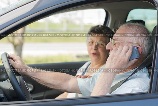 Elderly man on telephone while driving, wife in passenger seat. Стоковое фото, агентство Ingram Publishing / Фотобанк Лори