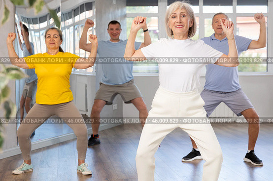 Elderly woman practicing Tai Chi with group in training room. Стоковое фото, фотограф Яков Филимонов / Фотобанк Лори