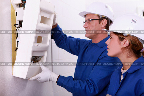 Electrician and apprentice mounting electric meter. Стоковое фото, агентство Ingram Publishing / Фотобанк Лори