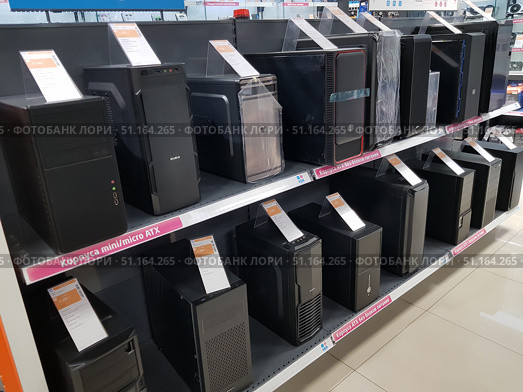 Electronics store display cases with personal computer cases. The shelves feature mini/micro ATX and ATX models without power supplies. The cases vary in design, size and functionality — from simple office solutions to modern gaming cases with decorative elements. Each product is provided with an information price tag with characteristics and cost. The display case is neatly decorated, which emphasizes the range and convenience of choosing components for assembling a computer. (2019 год). Редакционное фото, фотограф Анна Кривицкая / Фотобанк Лори