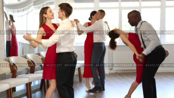 Elegant couple, smiling young guy and stylish woman in red dress enjoying slow foxtrot in dance studio. Amateur ballroom dancing concept. Стоковое видео, видеограф Яков Филимонов / Фотобанк Лори