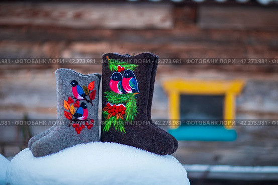 Embroidered felt boots taken on a winter evening against the background of snow, bushes and a village house (2020 год). Редакционное фото, фотограф Андриян Григорьевич Чаркин / Фотобанк Лори