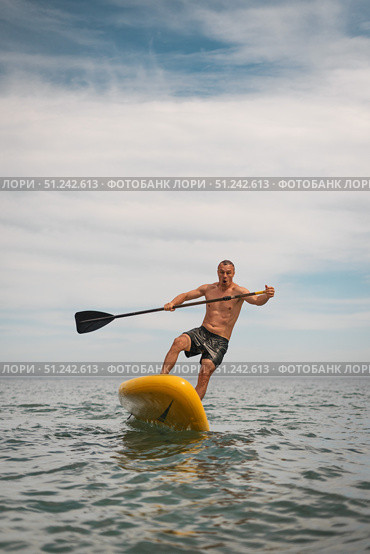 Energetic male on yellow paddle board tries to stay balanced while surfing waves. His joyful expression and intense movement capture freedom and humor of outdoor water sport. Стоковая иллюстрация, иллюстратор Енваев Андрей / Фотобанк Лори
