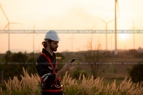 Engineers working on wind farms for renewable energy are responsible for maintaining large wind turbines. Review all tasks of the day while the evening sun shines a beautiful golden light upon both of them. Стоковое фото, агентство Ingram Publishing / Фотобанк Лори