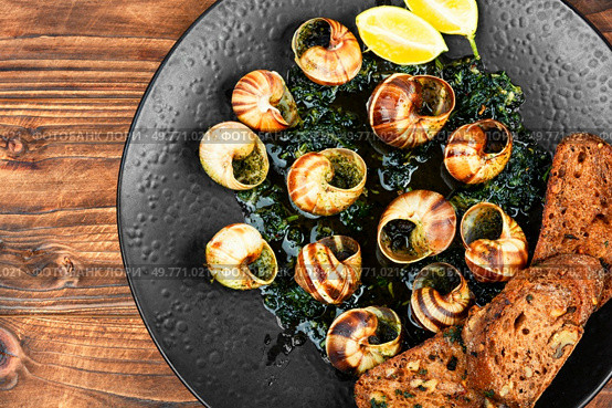 Escargot or snails seasoned with butter. Snails delicates on rustic wooden table.. Dish of snails in spicy sauce, Spanish food. Стоковое фото, агентство Ingram Publishing / Фотобанк Лори