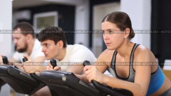 European is exercising on an exercise bike in the gym. Young woman focused while keeping pace on stationary bike. Стоковое видео, видеограф Яков Филимонов / Фотобанк Лори