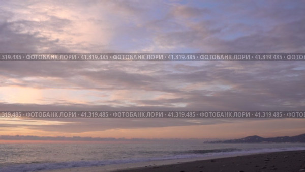 Evening. Sea. The sky is painted in pastel shades of pink and blue. The cape and city buildings are visible in the distance. Waves foaming on a pebble beach. A husky dog runs along the shore and hides. Стоковое видео, видеограф Вера Ивановна Кубарева / Фотобанк Лори