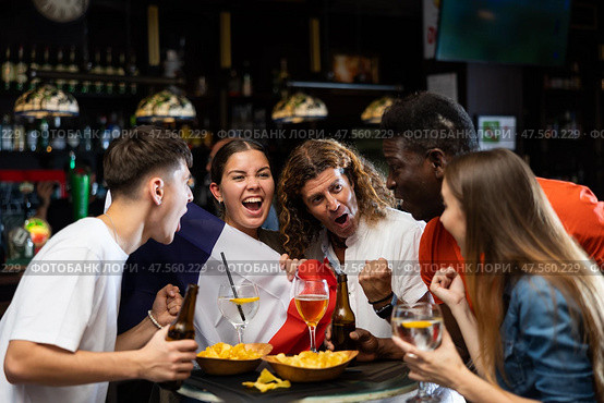 Excited diverse football supporters with flag of France watching tournament with beer and snacks in the pub. Стоковое фото, фотограф Яков Филимонов / Фотобанк Лори