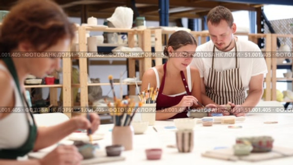 Experienced potter helps students learn how to make patterns on ceramic plates using paint and brush in a pottery workshop. Стоковое видео, видеограф Яков Филимонов / Фотобанк Лори