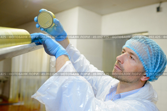 Factory worker refilling hopper of lids in machine. Стоковое фото, агентство Ingram Publishing / Фотобанк Лори