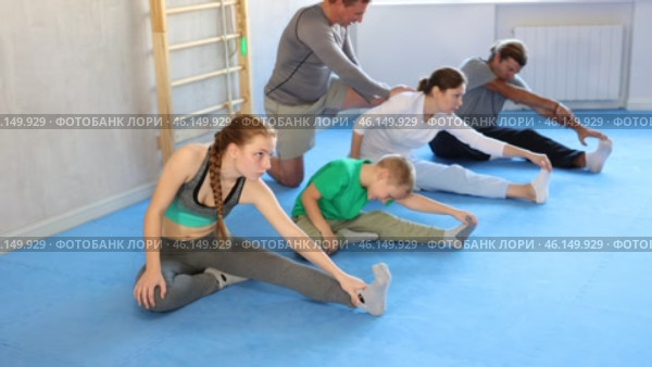 Family in gym during group sports training under guidance of trainer performs stretching on floor. Стоковое видео, видеограф Яков Филимонов / Фотобанк Лори