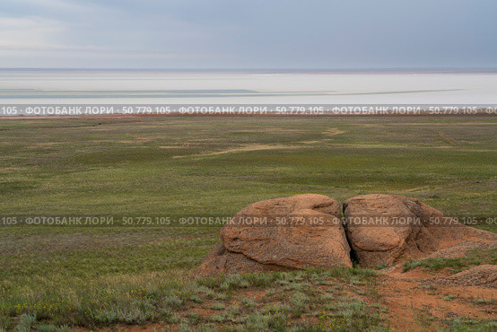 Fancy stones on the slopes of Bolshoe Bogdo Mountain and the salt lake Baskunchak in the distance on a summer day, Bogdinsko-Baskunchak Nature Reserve, Akhtubinsky district, Astrakhan region, Russia. Стоковое фото, фотограф Ula Ulachka / Фотобанк Лори