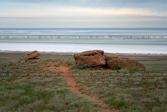 Fancy stones on the slopes of Bolshoe Bogdo Mountain and the salt lake Baskunchak in the distance on a summer day, Bogdinsko-Baskunchak Nature Reserve, Akhtubinsky district, Astrakhan region, Russia. Стоковое фото, фотограф Ula Ulachka / Фотобанк Лори