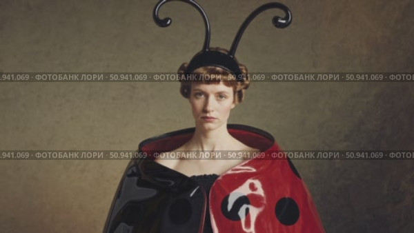 Fashion model wearing ladybug inspired costume with antennae and red and black polka dot cape posing in a studio setting with a textured background. Стоковое AI-видео, аниматор Данил Руденко / Фотобанк Лори