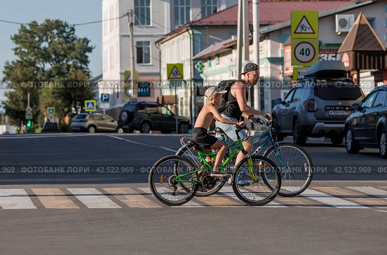 Father and son are riding around the city, riding bicycles. Middle-aged urban residents traveling by bike. People are driving along a pedestrian crossing in the city.Zaraisk, Russia, August 2023. Редакционное фото, фотограф Photojuli / Фотобанк Лори