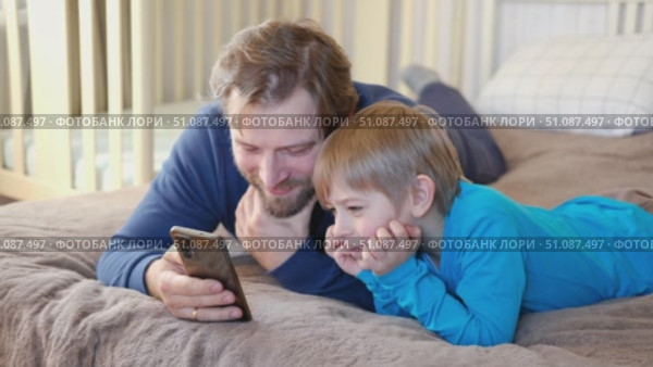 Father and son little boy laughing and using phone. They watching funny videos together, playing games on smartphone. Concept technology, smartphone addicted. Fun weekend activity. Modern fatherhood. Стоковое видео, видеограф Марина Демидюк / Фотобанк Лори