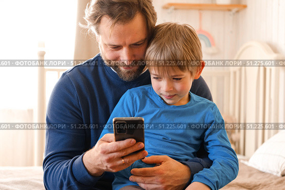 Father and son little boy laughing and using phone. They watching funny videos together, playing games on smartphone. Concept technology, smart phone addicted. Fun weekend activity. Modern fatherhood. Стоковое фото, фотограф Марина Демидюк / Фотобанк Лори