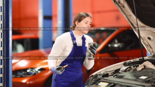 Female auto mechanic checking oil level in car engine in garage. Стоковое видео, видеограф Яков Филимонов / Фотобанк Лори