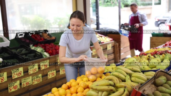 Female customer came shopping and stopped at crates of fruit and pick up orange for mulled wine. Стоковое видео, видеограф Яков Филимонов / Фотобанк Лори
