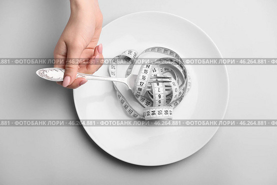 Female hand with plate, fork and measuring tape on grey background. Concept of anorexia. Стоковое фото, фотограф Pixel_shot / Фотобанк Лори