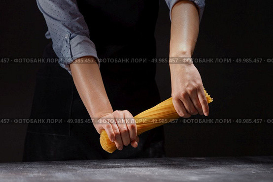 female hands clenching in fists bend, trying to break in half a bunch of raw long yellow thin spaghetti pasta on a black background. chef in an apron breaks a handful of raw Italian spaghetti. Стоковое фото, агентство Ingram Publishing / Фотобанк Лори