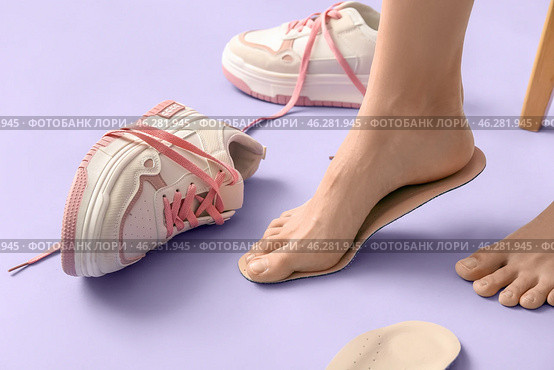 Female legs fitting orthopedic insoles near sneakers on lilac background, closeup. Стоковое фото, фотограф Pixel_shot / Фотобанк Лори