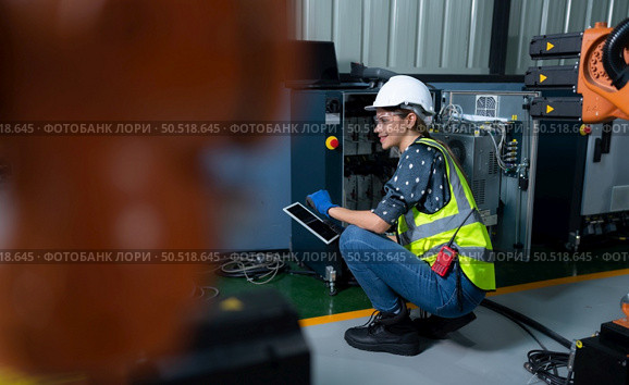 Female Technician Inspecting and repairing robotics arm in robots hangar and test the operation of the machine after being used for a while, as well as updating the software and calibration. Стоковое фото, агентство Ingram Publishing / Фотобанк Лори