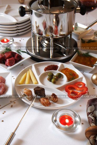 Festlich eingedeckter Tisch mit Fleischfondue. Weisse Tischdecke mit weissem Geschirr und weihnachtlicher Deko und Kerzen. Стоковое фото, агентство Ingram Publishing / Фотобанк Лори