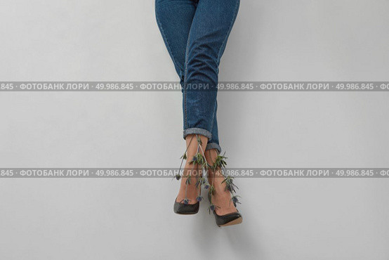 Flowers eryngium with woman legs in blue jeans on a gray background with copy space.. Woman legs with flowers eryngium in blue trousers on a gray. Стоковое фото, агентство Ingram Publishing / Фотобанк Лори