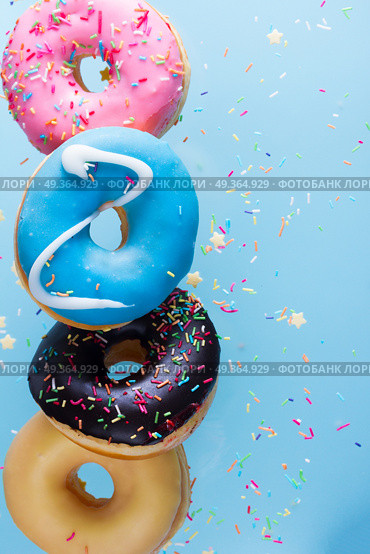 flying doughnuts on blue. flying doughnuts border - mix of multicolored sweet donuts with sprinkles on blue background. Стоковое фото, агентство Ingram Publishing / Фотобанк Лори