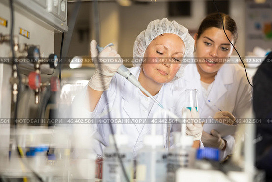 Focused female researchers mixing reagents in test tube with lab pipette while working in laboratory. Стоковое фото, фотограф Яков Филимонов / Фотобанк Лори