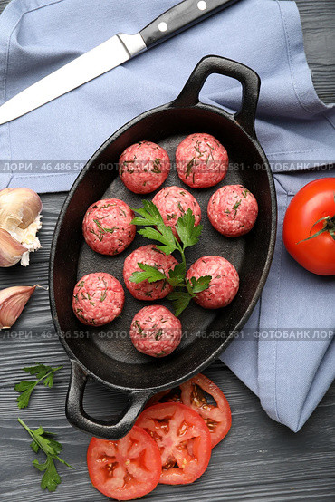 Форма для запекания с сырыми мясными шариками, овощами, ножом и салфеткой на темном деревянном фоне. Стоковое фото, фотограф Pixel_shot / Фотобанк Лори