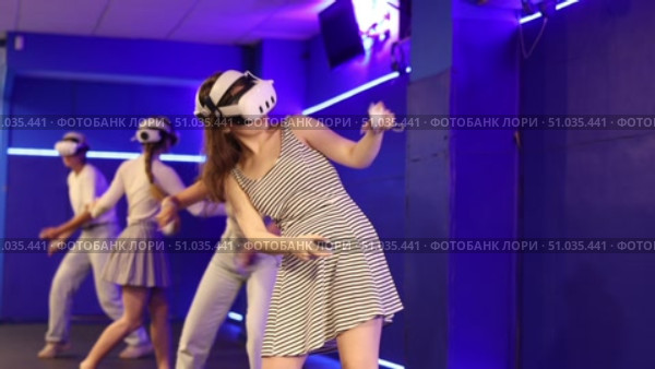 Four cheerful emotional young female friends in VR goggles standing in virtual reality room, manipulating objects or shooting at targets with gaming controllers in hands. Стоковое видео, видеограф Яков Филимонов / Фотобанк Лори