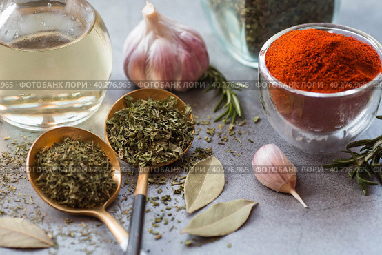 Fragrant spices. Dried parsley, dill, paprika, rosemary, garlic, bay leaf and a bottle of oil on a gray background. Free space. Стоковое фото, фотограф Photojuli / Фотобанк Лори