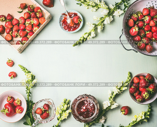 Frame made with fresh strawberries in colander and bowls with jam jar and spoon on kitchen table background with garden flowers, top view. Summer berries preserve concept. Seasonal local organic food. Стоковое фото, агентство Ingram Publishing / Фотобанк Лори