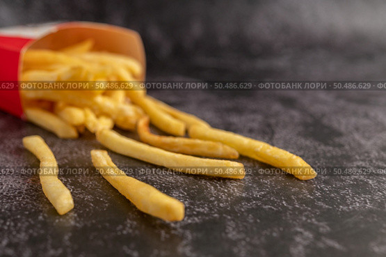 French fries poured out of a bag on a black cement floor. Стоковое фото, агентство Ingram Publishing / Фотобанк Лори