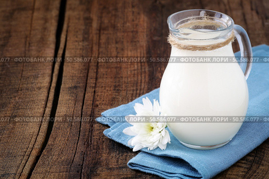 Fresh milk in a glass jug on a blue napkin with a chrysanthemum flower against dark rustic wooden background. Стоковое фото, агентство Ingram Publishing / Фотобанк Лори