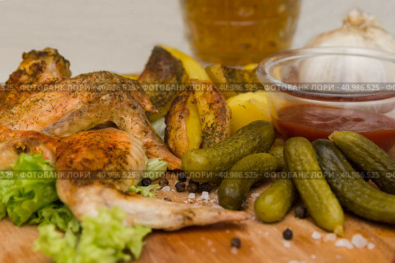 Fried chicken wings served on a wooden Board with Idaho potatoes, pickled gherkins and fresh lettuce leaves. A mug of beer is next to it. жареные куриные крылышки подаются на деревянной доске с картофелем Айдахо, маринованными корнишонами и свежими листьями салата. Рядом с ним стоит кружка пива. Стоковое фото, фотограф Дмитрий Березнев / Фотобанк Лори