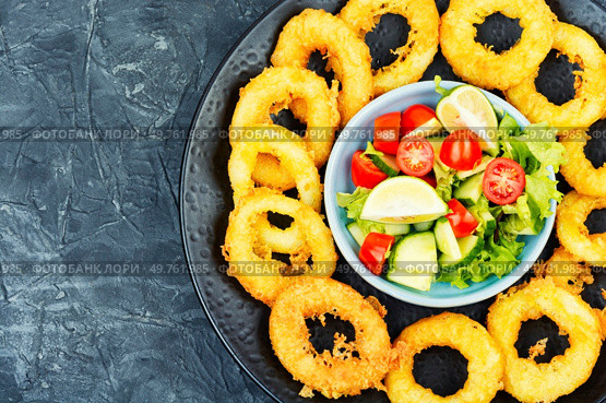 Fried squids or octopus (calamari) with fresh vegetable salad. Copy space.. Battered squid rings on plate. Стоковое фото, агентство Ingram Publishing / Фотобанк Лори